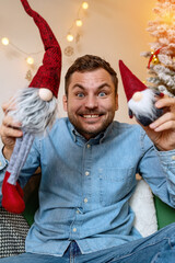 Obraz premium Childishness of adult people while Christmas. Young adult happy man playing with kids toy gnomes.