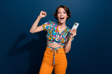 Photo of young amazed girl brown bob hair raised fist up holding smartphone win lottery prize in internet isolated on blue color background