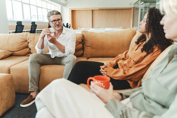 Portrait of confident businesspeople sitting on comfortable sofa holding cup drinking drink enjoying