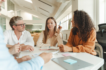 Confident businesswoman sitting at workplace working with colleagues, brainstorming, sharing ideas
