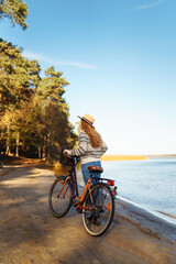 Fototapeta premium A beautiful woman in a hat and sweater rides a bicycle in an autumn park. Active tourist enjoying sunny weather. Weekend concept. Active lifestyle.