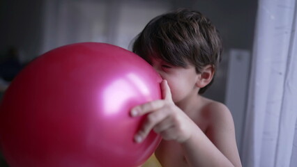 One fun child blowing up balloon with mouth. Happy small boy biting balloon with teeth
