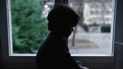 Melancholic child sitting by window at home feeling sad and depressed