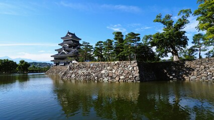 Fototapeta na wymiar Matsumoto Castle and trees at riverside with water reflection on a sunny day with bright blue sky in Japan
