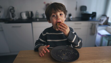 Child eating piece of bread at kitchen table, adorable 4 year old boy snacking carb food on plate