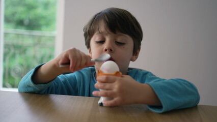 Child breaking soft boiled egg with spoon, preparing to eat oeuf a la coque. Close-up kid hitting the surface of healthy snack