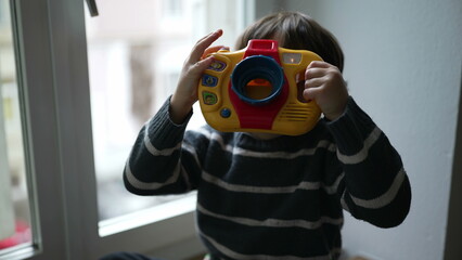 Child pretending to take photo with toy photography object in hand. Fun happy little boy playing at...