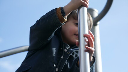 Joyful child sliding down metal bar at playground structure. Fun little boy enjoying outdoor...