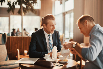 Two Caucasian middle aged businessmen having a meeting over some coffee in a café decorated for Christmas and the new year holidays