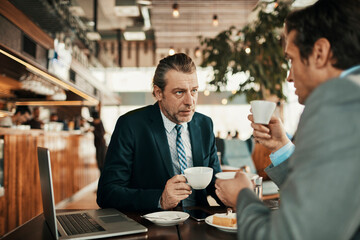 Pair of businessmen enjoying coffee and conversing about work together in a cafe