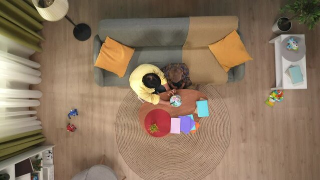 Top view of grandmother grandson sitting in the room, woman showing boy a globe, they spin look at map and talk.