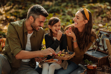 Mother, father and daughter eating their food during forest picnic - obrazy, fototapety, plakaty
