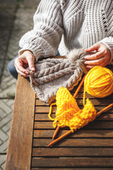 Woman holding handmade knit hat. Yellow ball of wool and knitting needle on table