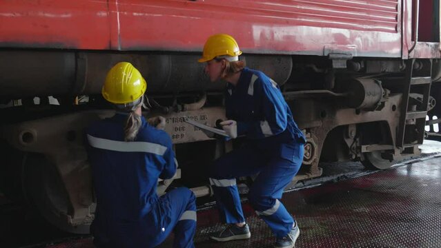 Young caucasian engineer man and woman maintenance and repair train diesel engine in station, team engineer inspect system transport, technician checking infrastructure, transportation and industry.