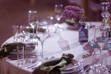 A table setting in a restaurant with a white tablecloth, a green napkin, a small vase with purple flowers, and various glasses. Concept for illustrating fine dining or hospitality services.