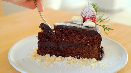 Man hand taking a bite of moist, delicious chocolate cake with a spoon. Closeup of rich, dark chocolate cake with chocolate mousse and chocolate glaze. Dessert for birthday party or special occasion.