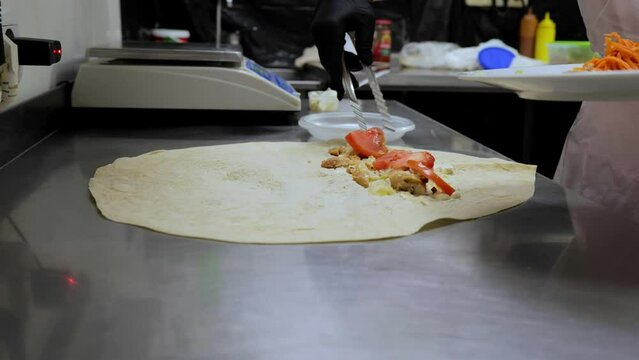 Shawarma in pita bread, shawarma pita vegetables fried potatoes cabbage onions, close-up of the process of cooking shawarma in pita bread, cooking tongs put vegetables on pita bread.