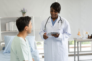 Caucasian patient man use tablet computer and talk with African American doctor woman at hospital