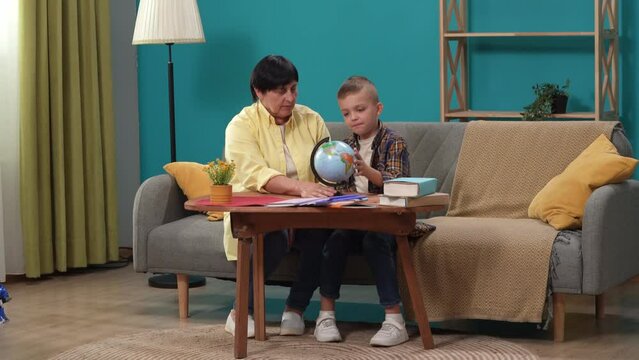 Close up shot of grandmother grandson sitting on sofa, woman showing boy a globe, he spins it looking at the map.
