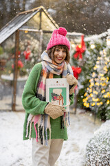 Portrait of a young woman holding magazine with New Year's cover at snowy backyard decorated for a winter holidays