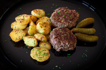 ready for eat - grilled venison burger, fried potatoes, pickles and chives served on a black plate