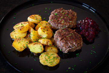 ready to eat - grilled venison burger, homemade cranberry marmalade and fried potatoes on a black plate