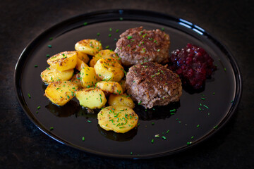 ready to eat - grilled venison burger, homemade cranberry marmalade and fried potatoes on a black plate