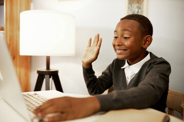 Side view of cute black boy in school uniform greeting his classmates in virtual classroom sitting in front of laptop smiling and waving hand at screen, studying online from home. Distant learning - obrazy, fototapety, plakaty
