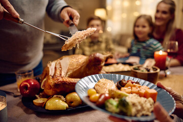Close up of man carving Thanksgiving turkey during family meal at dining table.