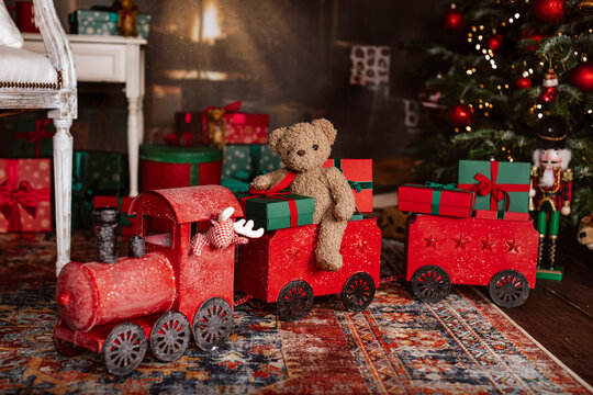 Teddy bear in a red Christmas train under the christmas tree by the fireplace