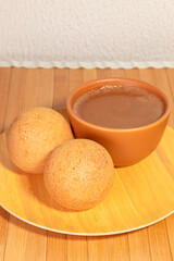 Two delicious Colombian buñuelos made of fried flour dough next to a cup of chocolate on a wooden plate. Typical food concept.