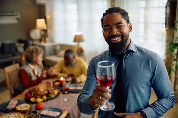 Happy black man toasting during family gathering on Thanksgiving and looking at camera.