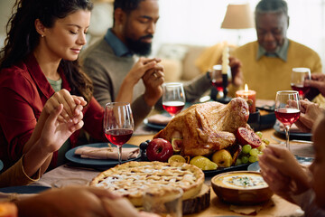 Close up of roast turkey with family praying at dining table during Thanksgiving meal.