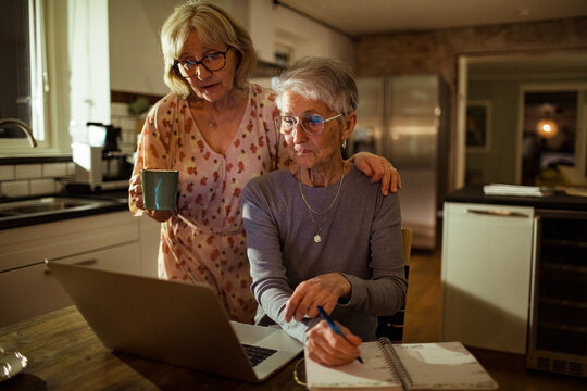Senior lesbian couple writing down notes from a laptop at home