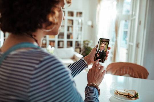Back view of a woman consulting her psychiatrist on a smartphone video call at home