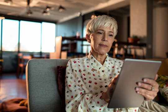 Mature woman using a tablet on the couch at home - Powered by Adobe