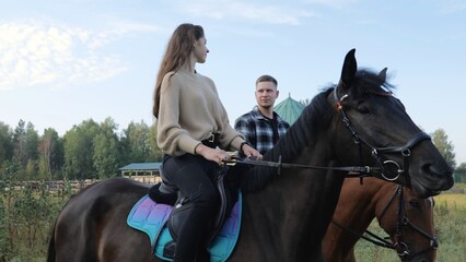 Obraz premium Training hobby during the holidays. Horseback riding at the farm, equestrian club. A young family rides horses. Riding lessons, a young couple ride horses in a paddock at a ranch.