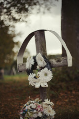 Old wooden cross headstone with flowers on traditional European cemetery. Close up of aged cross head stone on grave yard in the evening. Autumn scene. Single cross gravestone with floral decoration
