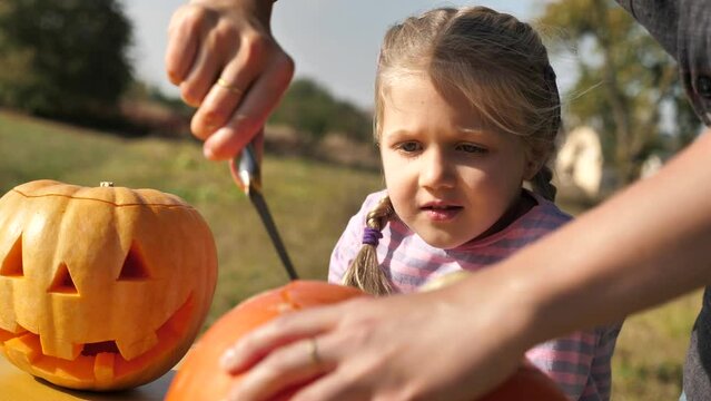 a blond child girl watches a woman carve a Halloween pumpkin. family traditions on Halloween