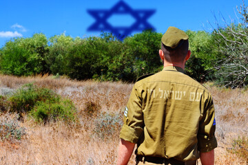 Fototapeta premium Israeli soldier with a patriotic inscription on his back opposite a blurry Jewish star. Translation of text from Hebrew - The people of Israel live. Concept: Israel will not allow a second Holocaust