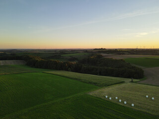 Aerial view of a countryside with agriculture fields and forest trees while the sun goes down 