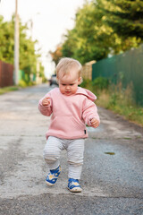 Caucasian baby child girl walks on wet asphalt and smiles