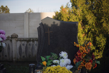 Blank headstone in the Christian cemetery. Close up of a single empty tombstone at European graveyard. Place for text on gravestone. Tombstone with flower decoration and trees. Autumn scene