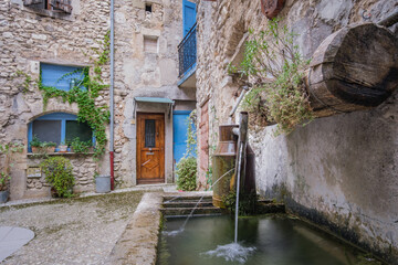 Fototapeta na wymiar Old stone house fa¸çade with blue shutters and fountain in the medieval village of Chatillon En Diois in the south of France (Drome)