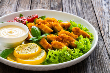 Caesar salad - fried breaded chicken breast and vegetables on wooden table
