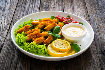 Caesar salad - fried breaded chicken breast and vegetables on wooden table
