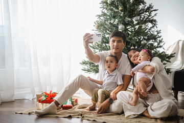 Asian family taking a selfie photo by using a smartphone while celebrating Christmas in the living...