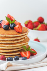 Stack of fresh pancakes with strawberries and blueberries drizzled with maple syrup and honey. Healthy traditional American breakfast on the white background