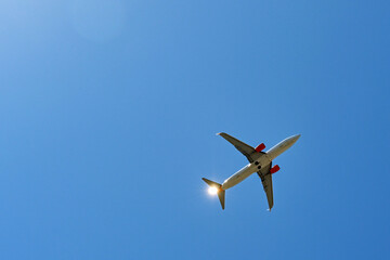 Modern passenger jet in flight isolated against a blue sky with the sun shining at the aircraft's tail