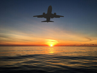 Silhouette of a holiday jet approaching a holiday resort over the sea at sunrise. Travel concept.